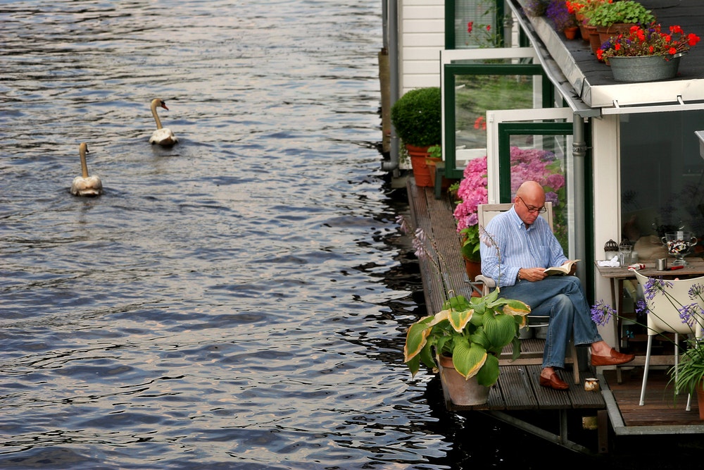 A man reads a book outdoors on a houseboat.