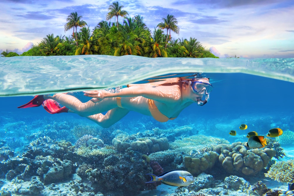Ung kvinne som snorkler i tropisk vann