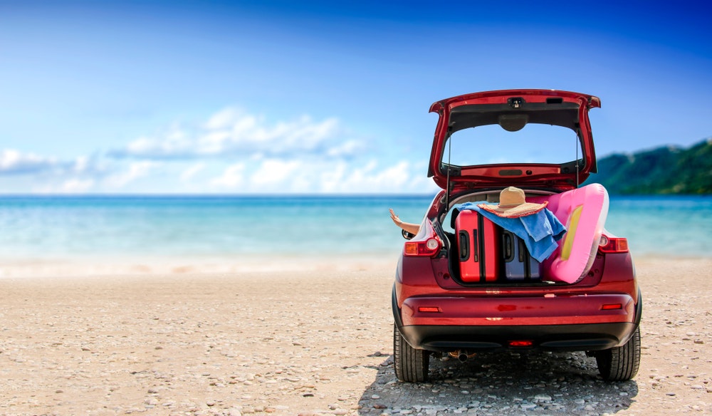 Summer time and a red car on the beach with several suitcases.