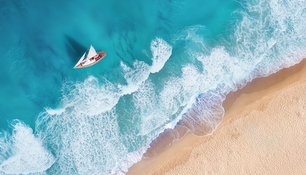 Waves and a yacht seen from above. Turquoise water background seen from above.