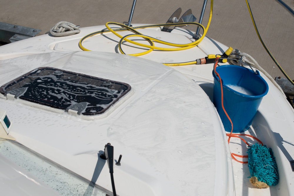 Boat cleaning equipment. Plastic bucket, hose with water spray, mop lying on the yacht.