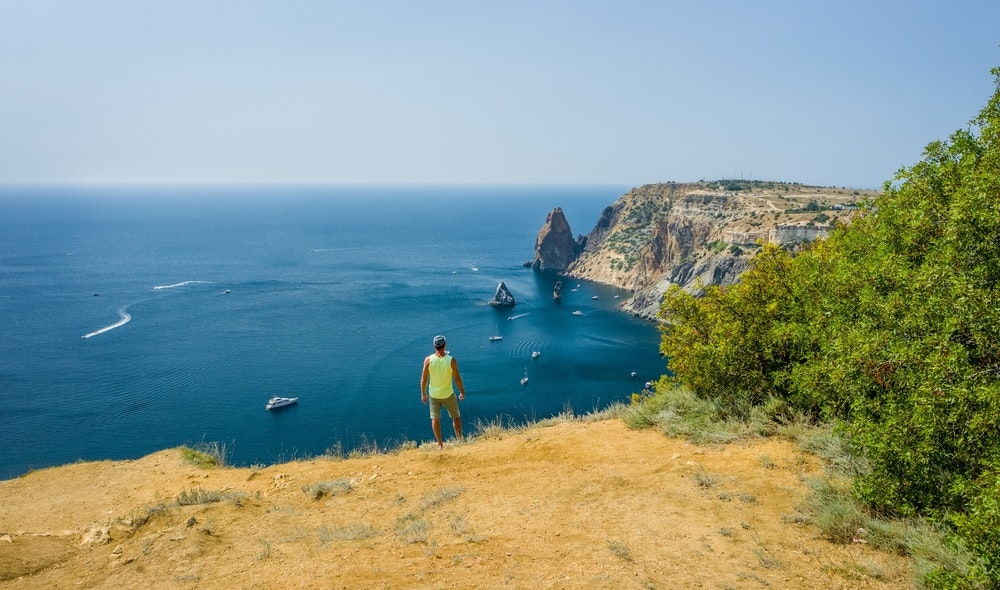 A man hiking on the cliffs at the seashore, view of boats in the bay.