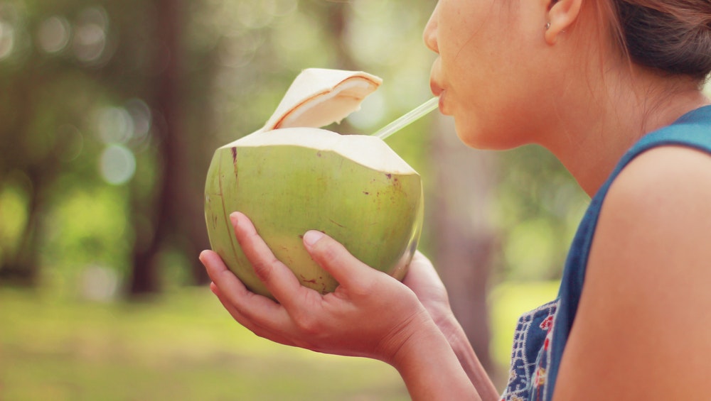 Dívka pije kokosovou vodu přímo z kokosu