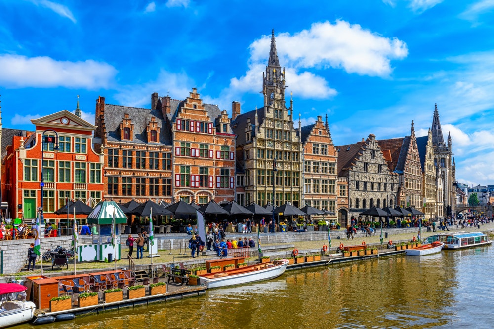 Malebné městečko Gent, Belgie s vodním kanálem, loďkami a nábřežím.