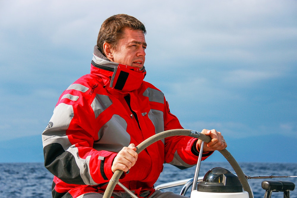 A sailor in a sports jacket at the helm of a racing sailboat