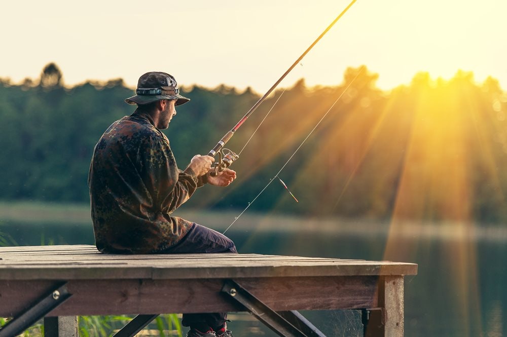 Rybář sedící na dřevěném molu v klobouku při západu slunce