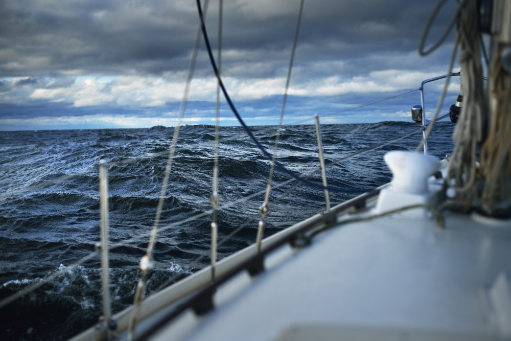 Bouřlivé počasí, vlny a mraky. Bílá jachta plující na otevřeném moři.