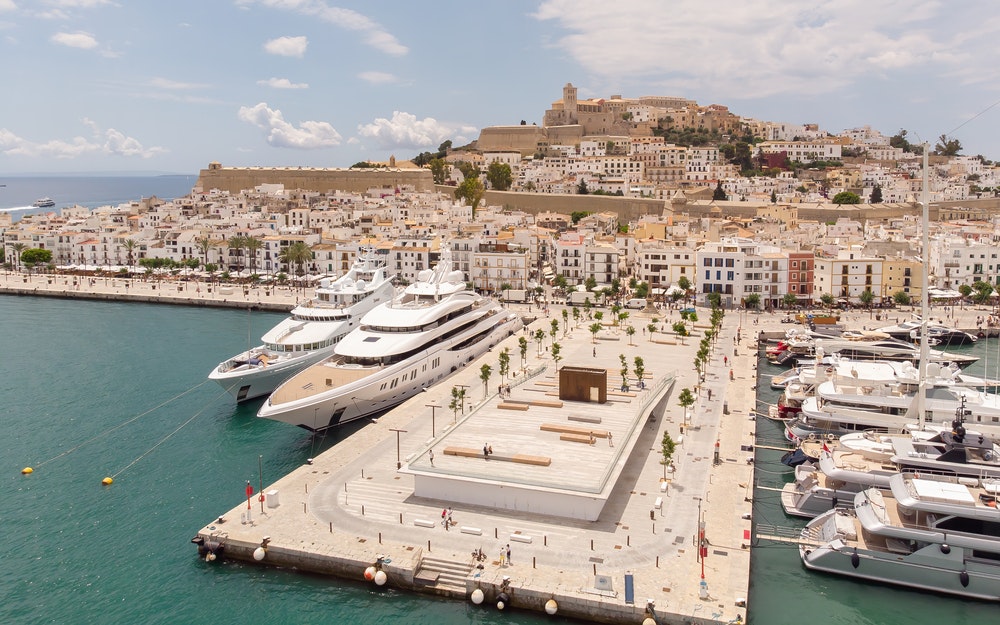 Přístav na Ibize s luxusními jachtami a akropolí Dalt Vila v pozadí 