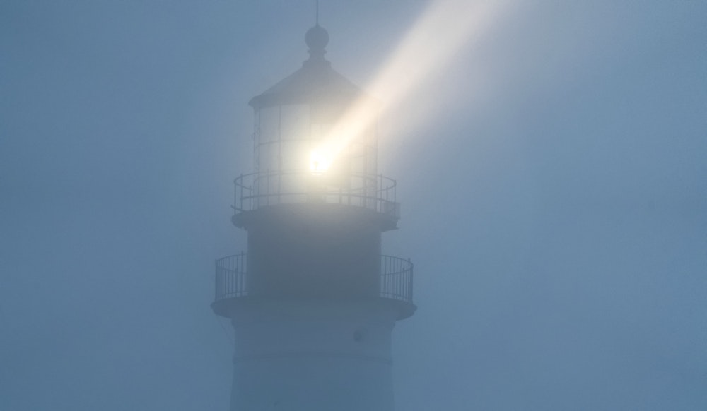 Beams of light from the lighthouse reflecting in the mist in the darkness.