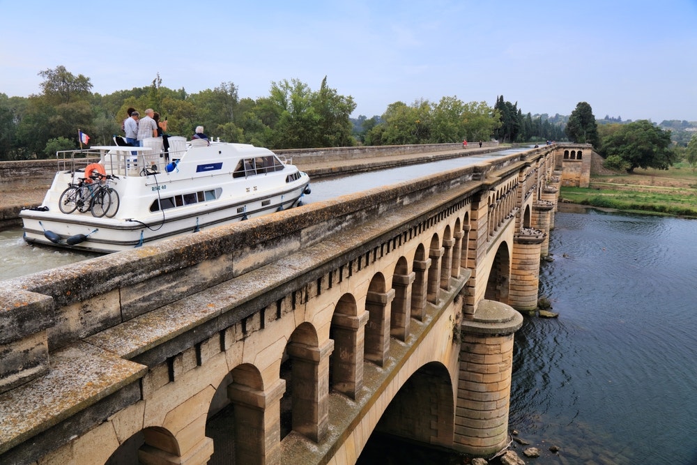 A boat crossing the bridge over the River Orb on the historic Canal du Midi in France. The Canal du Midi is a UNESCO World Heritage Site.
