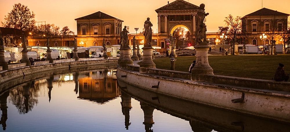 Náměstí Prato della Valle ve městě Padova, při západu slunce, vodní kanál, sochy