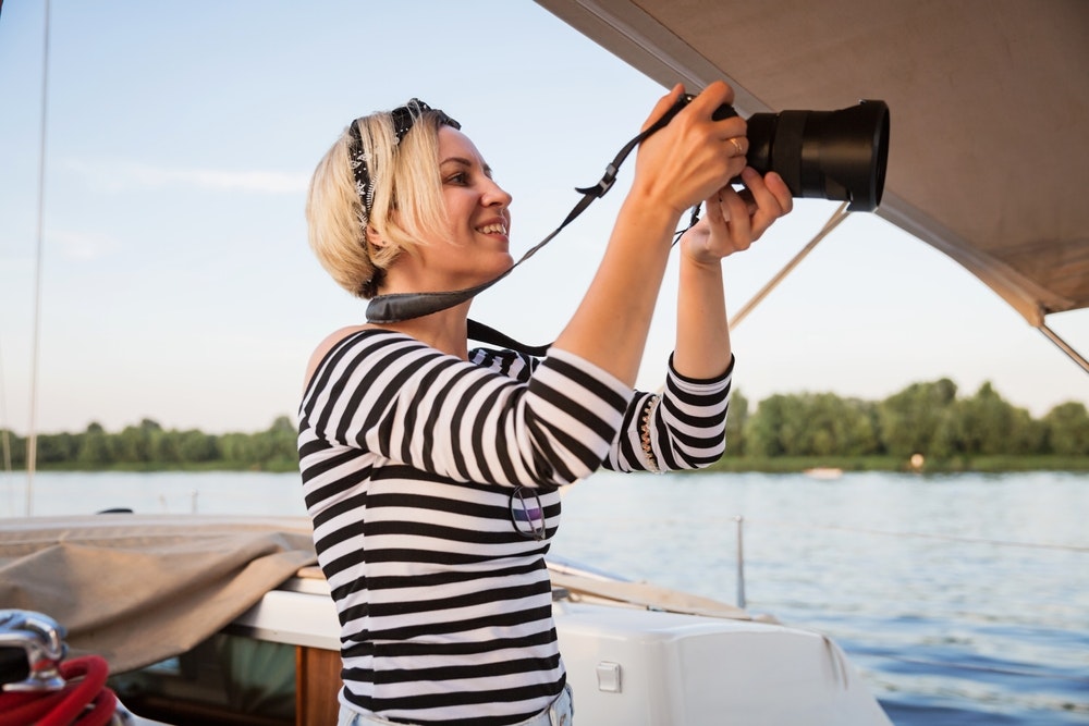 Μια γυναίκα με ένα ριγέ ναυτικό πουκάμισο κρατά μια κάμερα σε μια βάρκα.