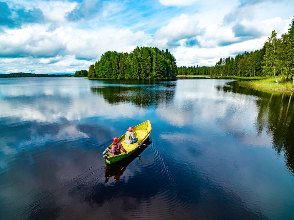 Žvejybinės valties su jauna moterimi ir vyru vaizdas iš oro žydrame vasaros ežere Suomijoje