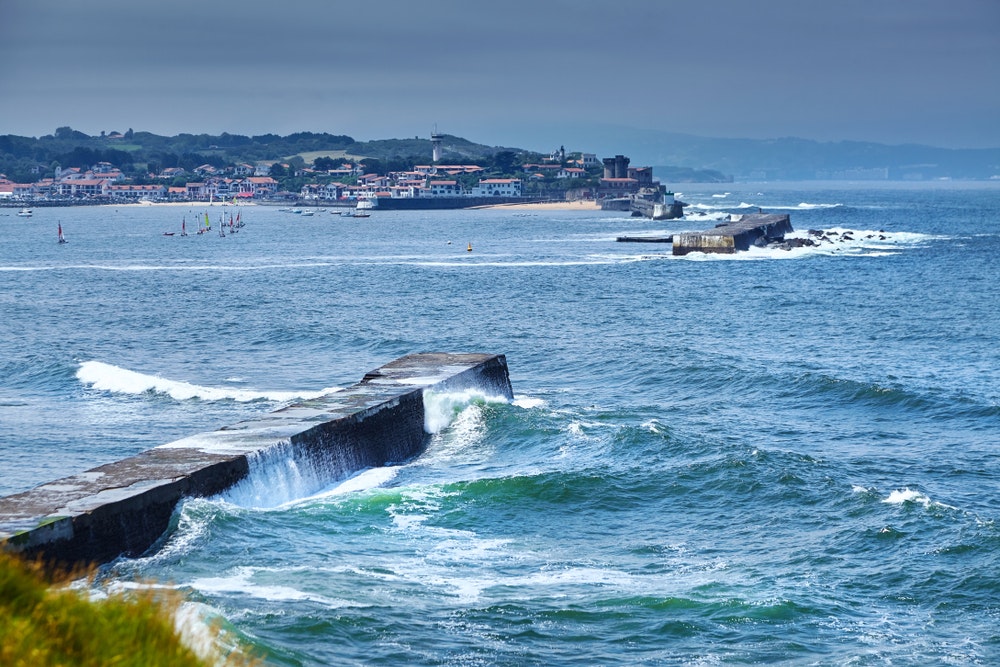 Views of the town of Ciboure and the castle and port of Socoa. Ocean waves crashing against the causeway