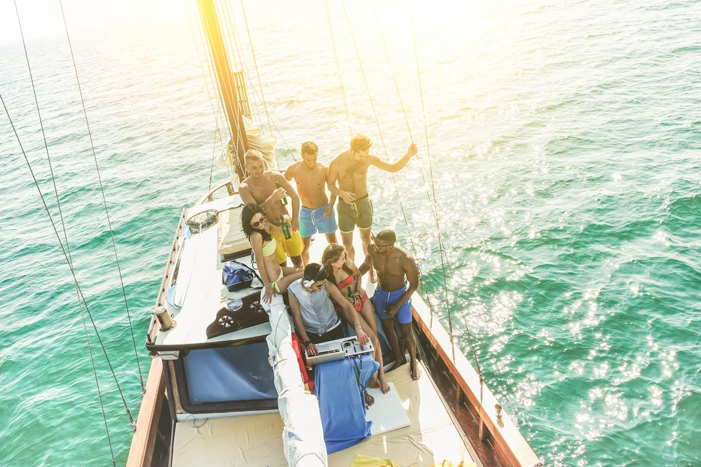 A group of young people drinking and dancing at a party on a sailboat with a DJ playing music