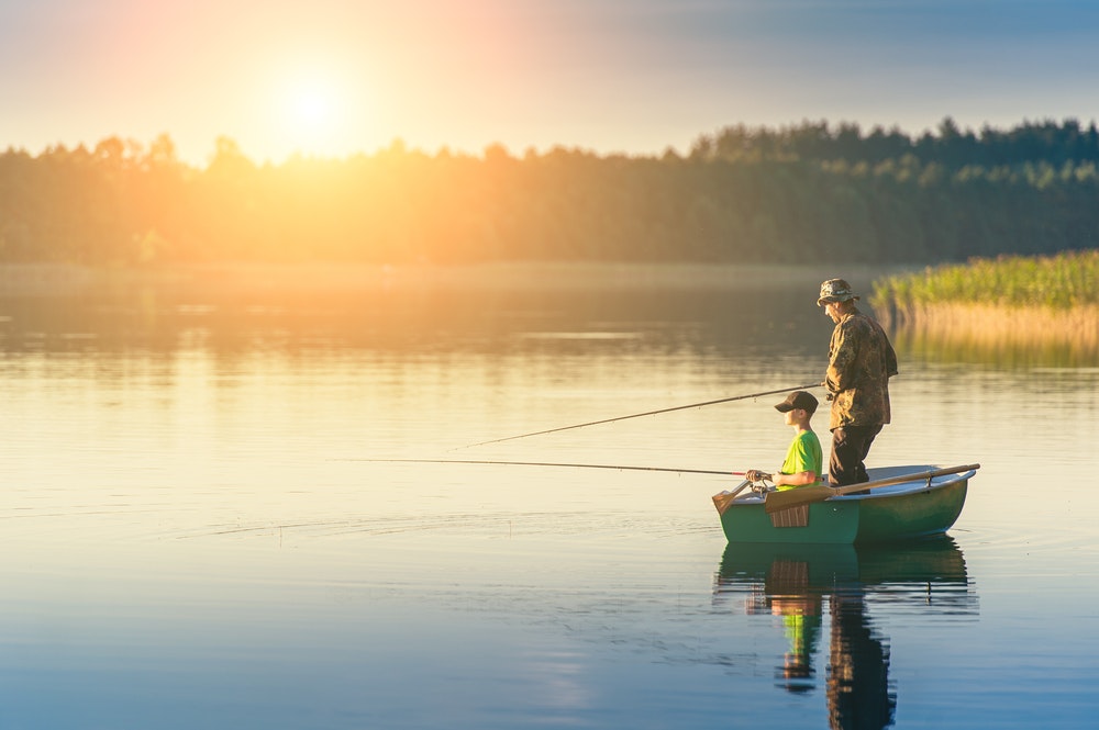 otec a syn loví ryby z lodi při západu slunce