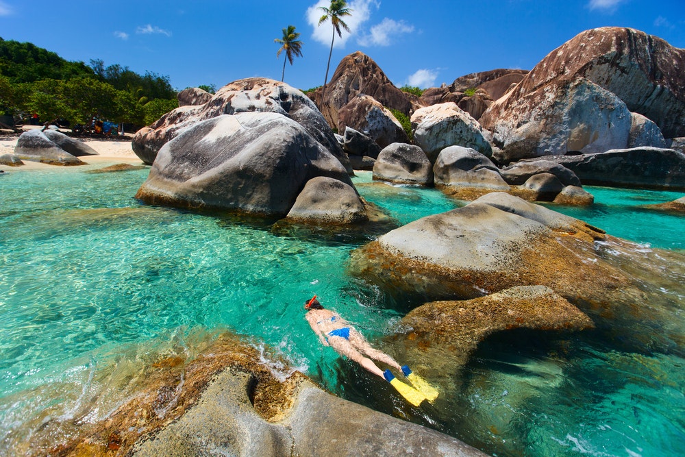Mladá žena šnorchluje v tyrkysové tropické vodě mezi obrovskými žulovými balvany na pláži The Baths, hlavní turistické atrakci na ostrově Virgin Gorda, Britské Panenské ostrovy, Karibik.