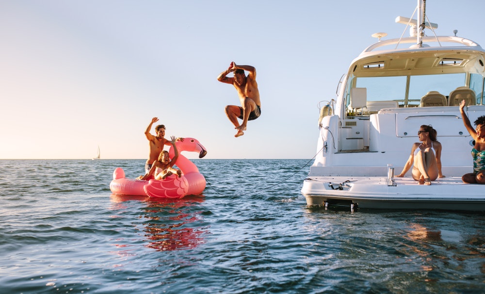 Group of friends, summer day on a yacht, jumping into the water, inflatable flamingo.
