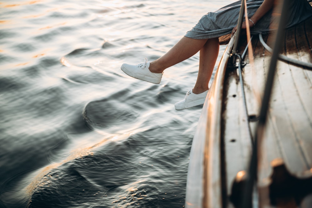 Merginos baltais sportbačiais, sėdinčios jachtoje, besimėgaujančios saulėlydžiu, kojos