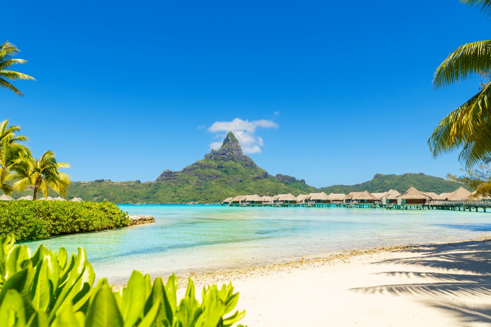 Bora Bora, Tahiti, Fransız Polinezyası tropikal adasında su üzerinde turkuaz lagünün ve bungalovların karşısındaki Otemanu Dağı'nın bir görünümü.