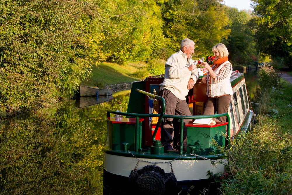 Una coppia di anziani su una pittoresca casa galleggiante con un bicchiere di vino
