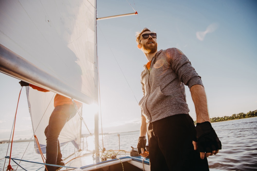 Young sailor wearing sunglasses and gloves on a sailboat at sunset.