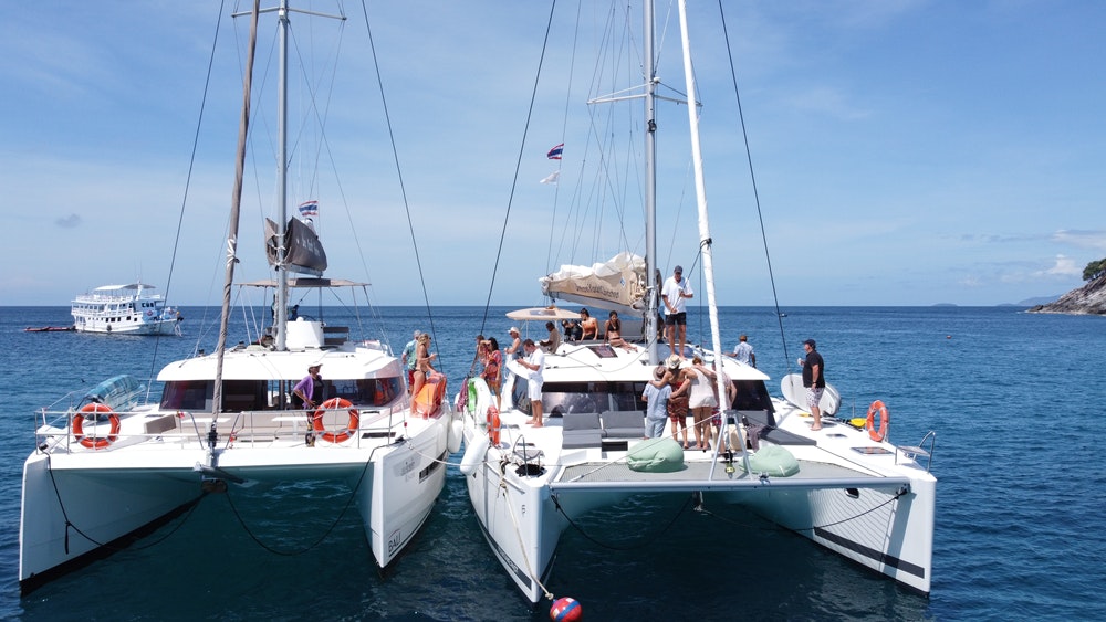 Two catamarans moored side by side with a bunch of people