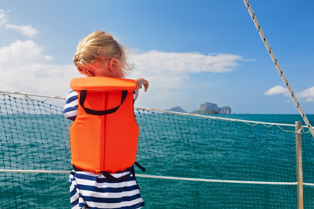 A child in a life jacket on the deck of a ship near the safety net.