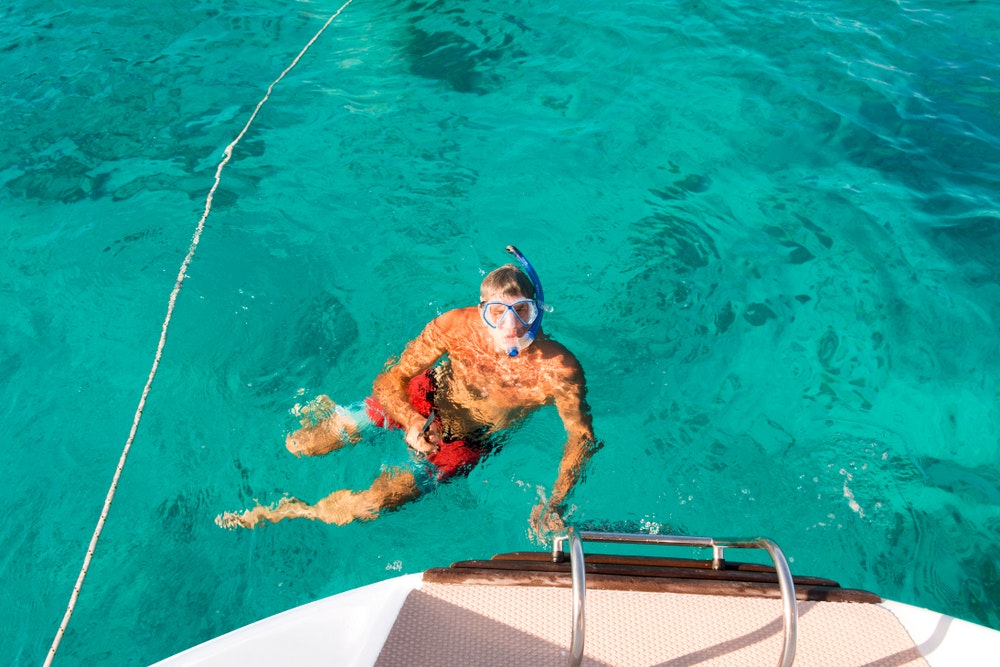 A man in the water at the stern of a boat with a snorkel and goggles. 