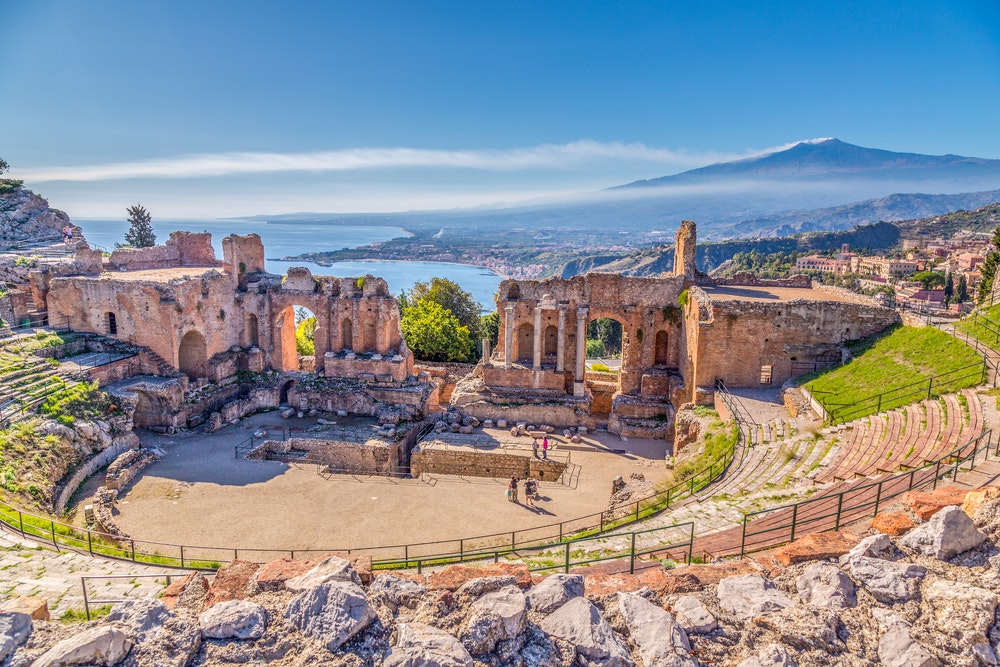 The ruins of an ancient Greek theatre in Taormina, Sicily, with the smouldering volcano Etna in the background. 