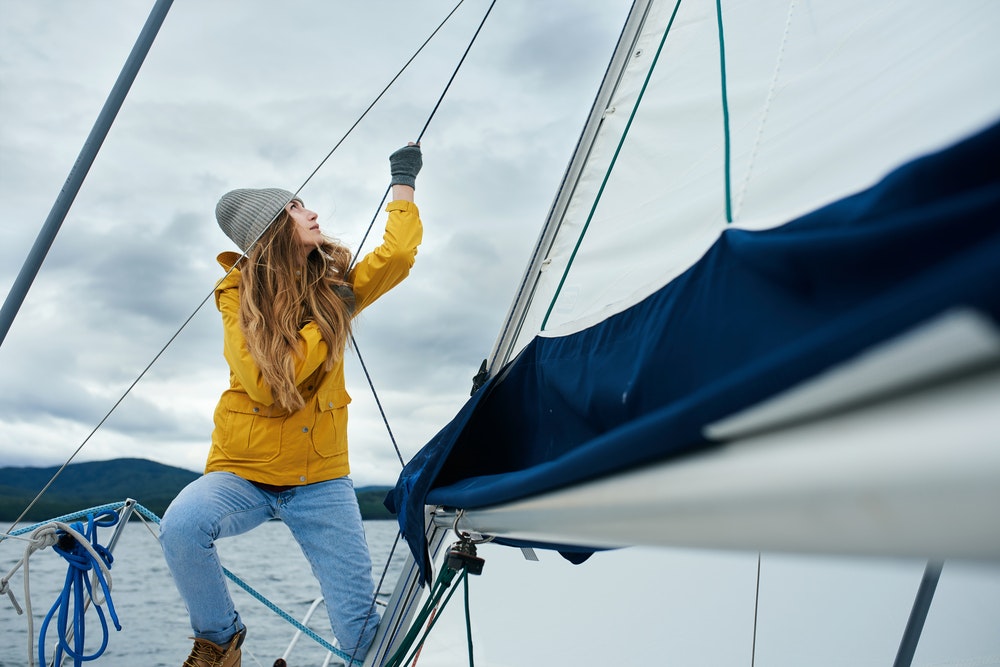 Mladá žena ve žluté bundě a čepici držící lano na lodi