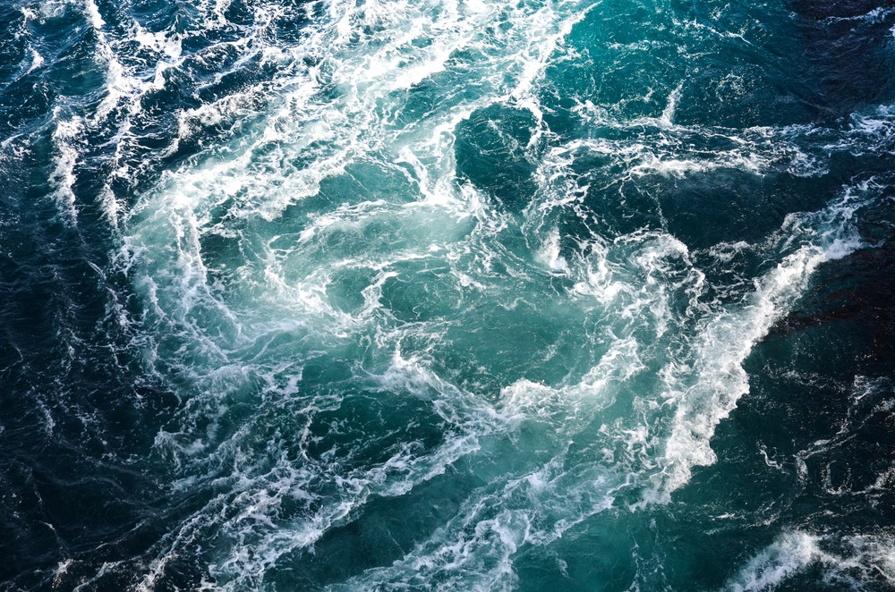 Bølger av sjøvann møter de spisse steinene under vann og skaper virvler.