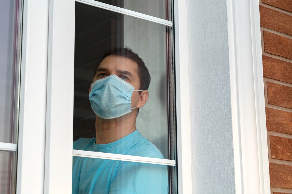 Karanténní sebeizolace. Muž v lékařské masce u okna.