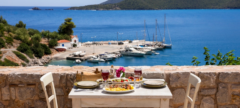 Bord servert for to med kyllingsouvlaki og chips, gresk salat, snacks og drinker på sommerterrassen
