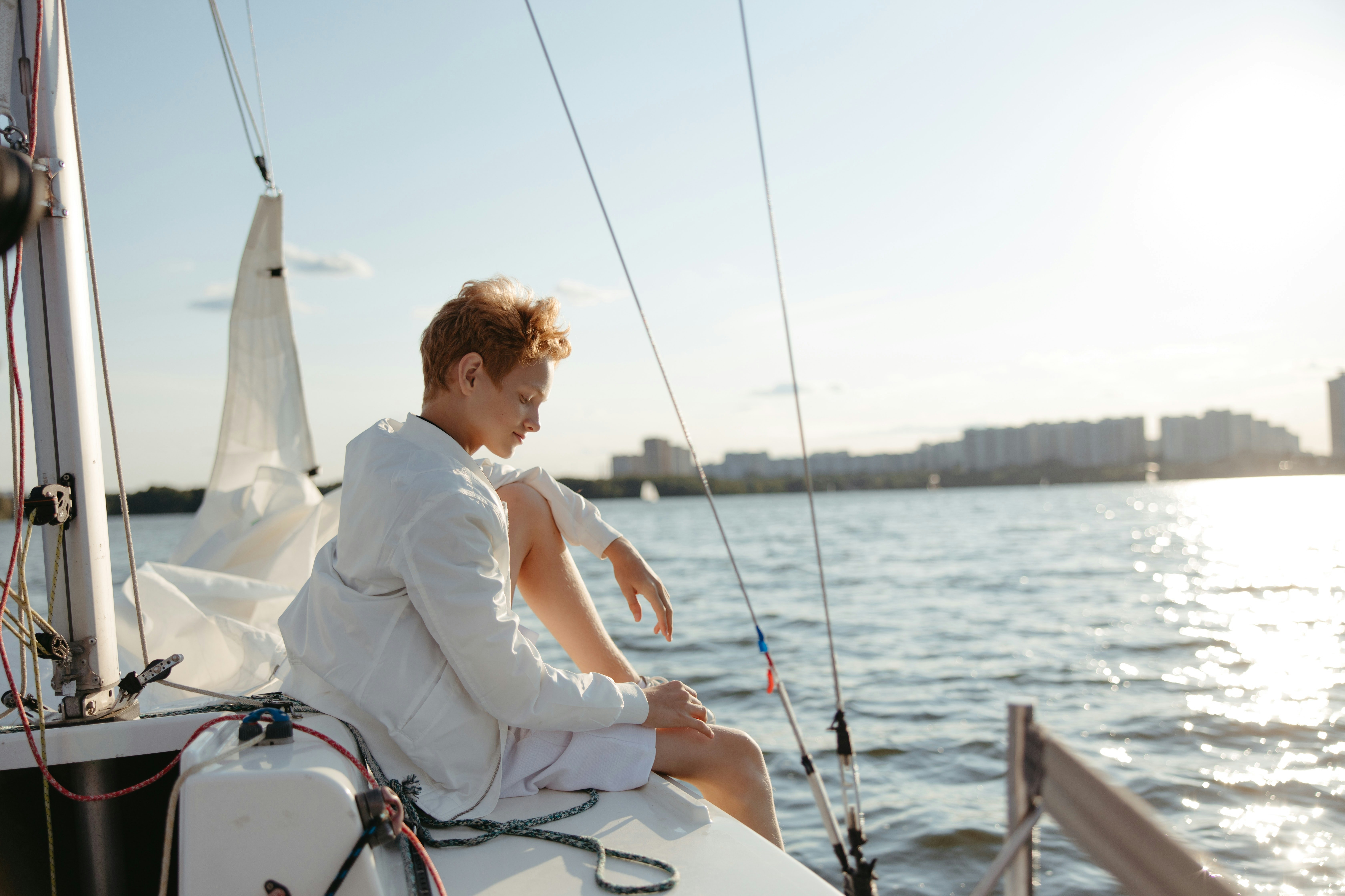 A lady or lady sitting on the bow of the boat in a white shirt and wind