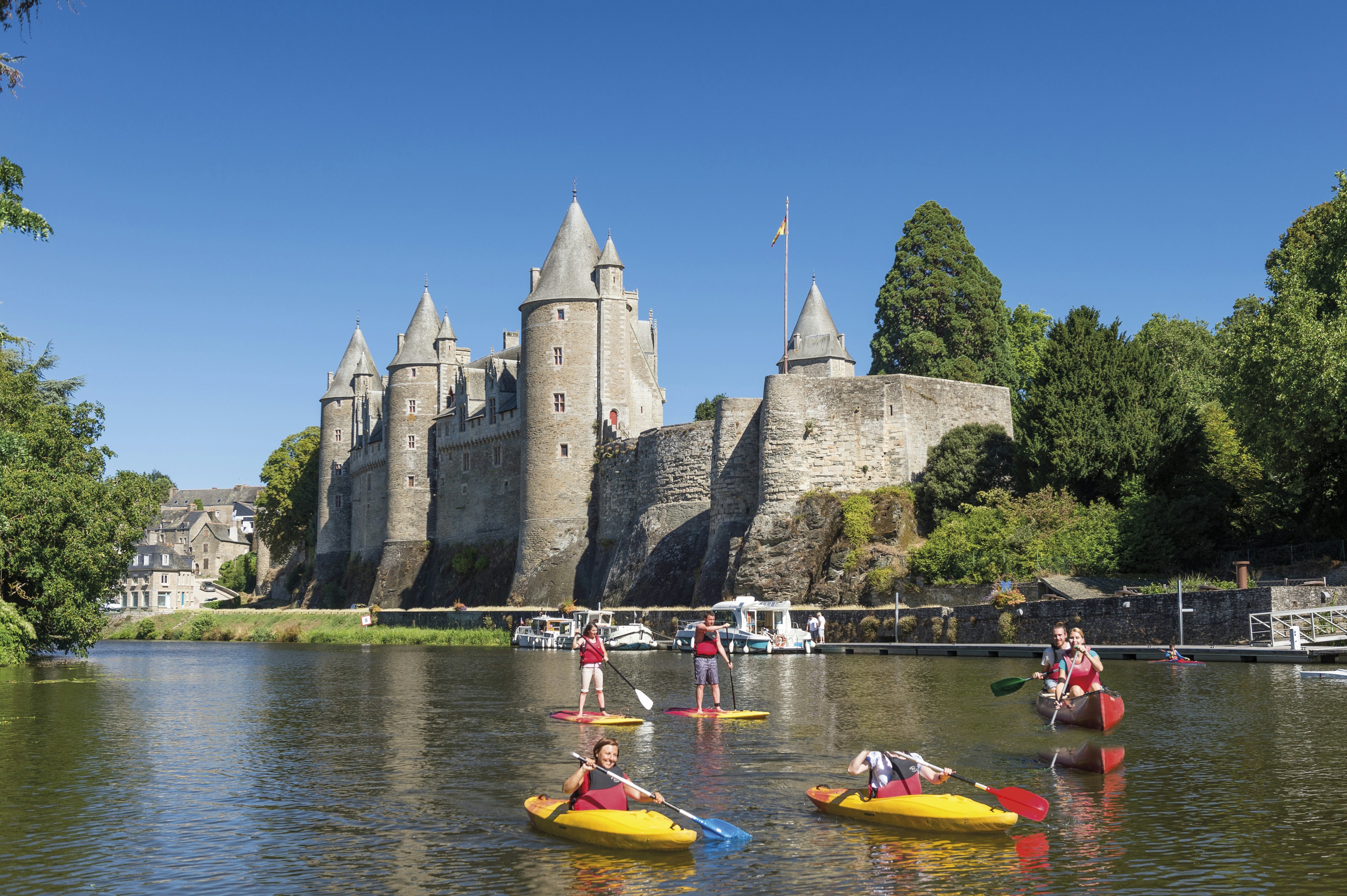 People on paddleboards and in kayaks on a quiet water channel in the foothills of Josselin Castle