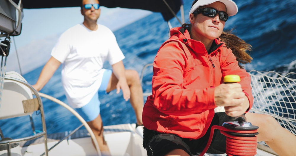 Yelkenli bir teknede spor giyimli ve güneş gözlüklü bir kadın.