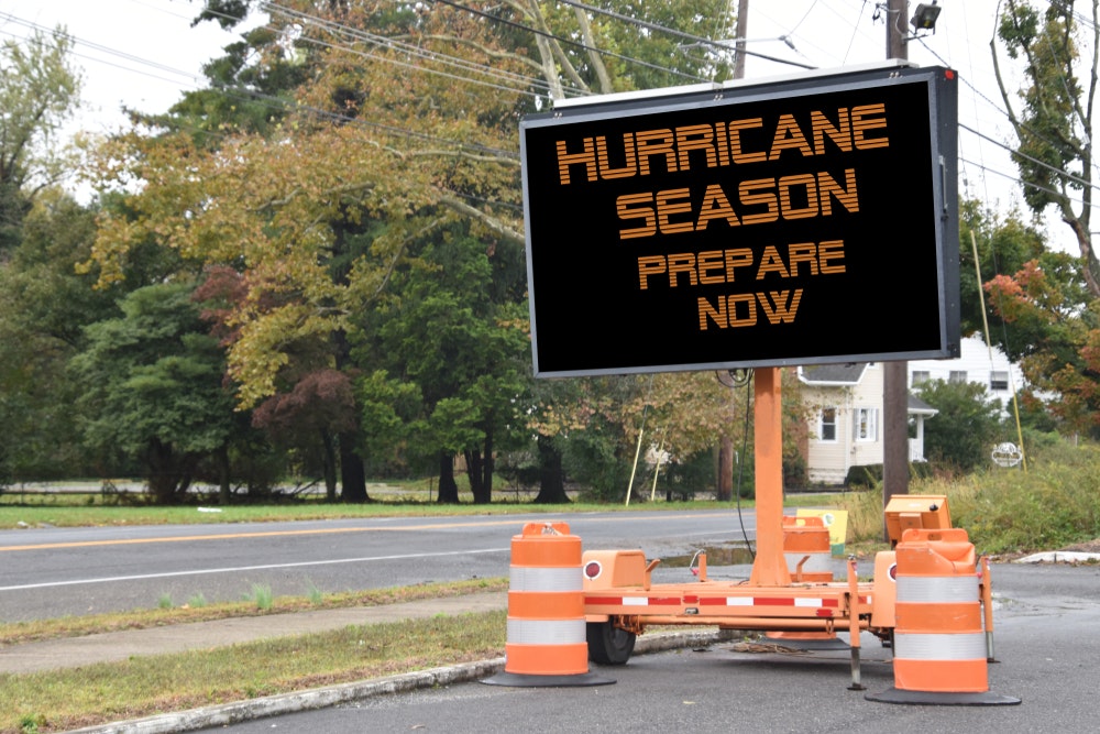 Digitální elektronická mobilní dopravní značka s nápisem Připravte se na hurikánovou sezónu, umístěná u silnice lemované stromy v sousedství.