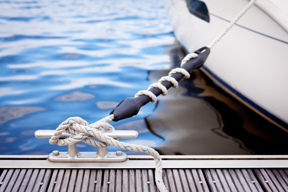 A white yacht moored with a line tied around a snubber to a dock cleat.
