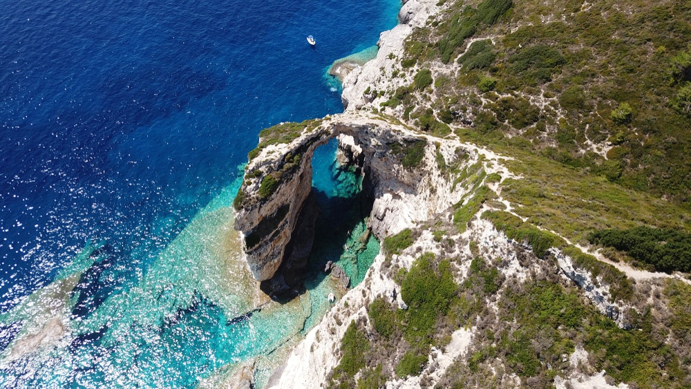 Et fugleperspektiv av en steinbue med turkist vann på øya Paxos, Det joniske hav, Hellas