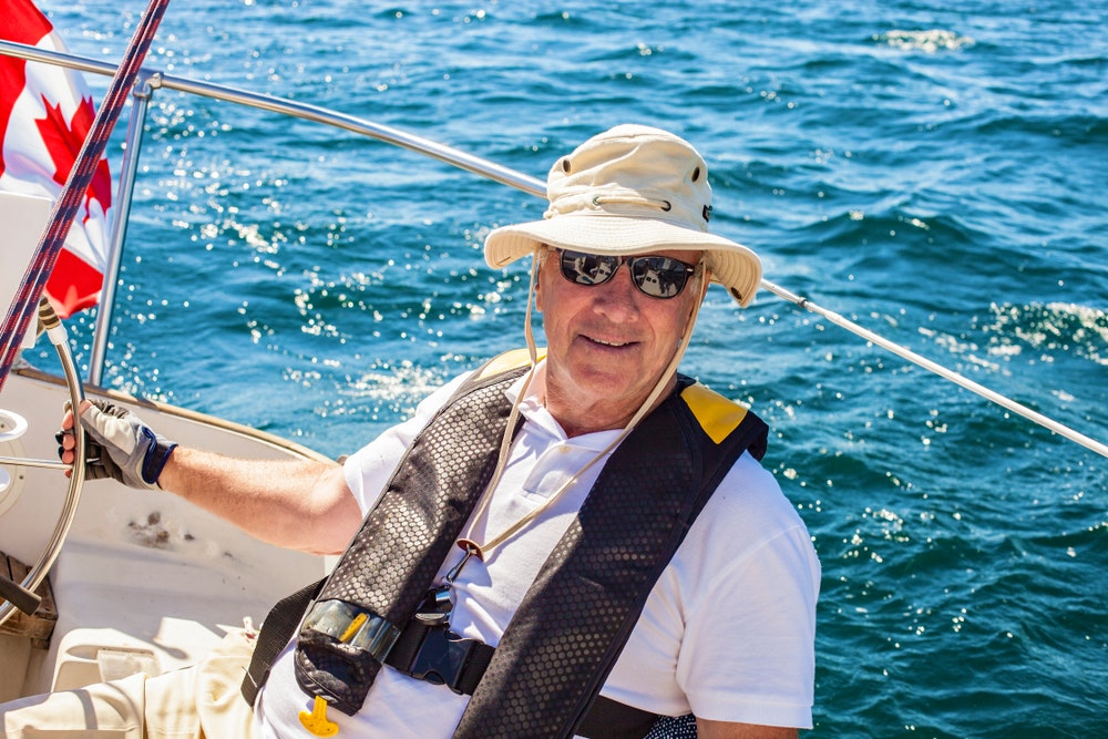 Starší námořník řídí plachetnici za slunečného letního dne. 
