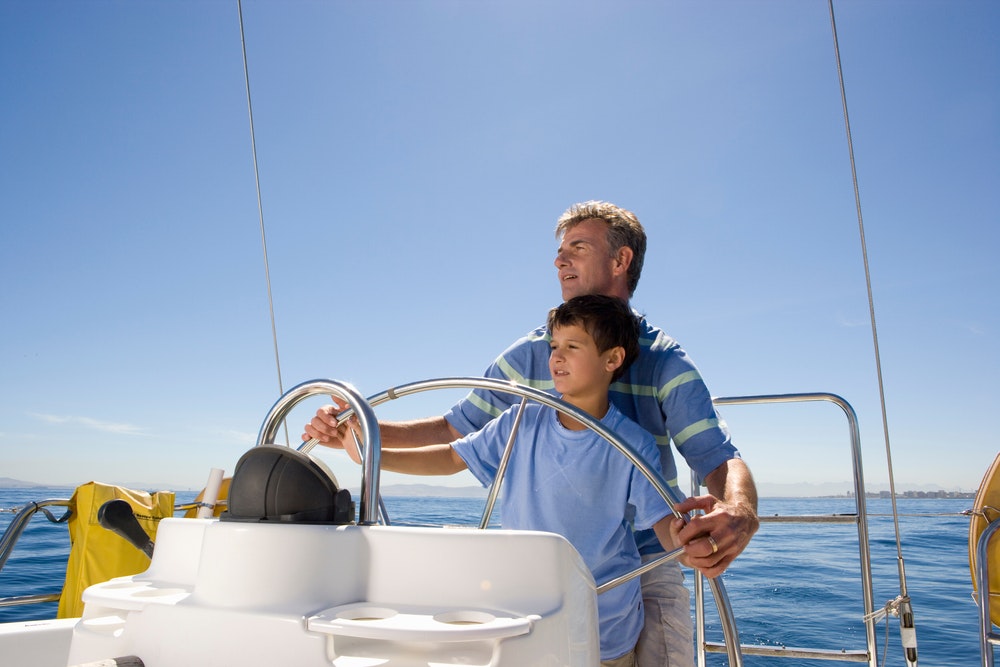 En far og sønn styrer en båt på en klar solskinnsdag.