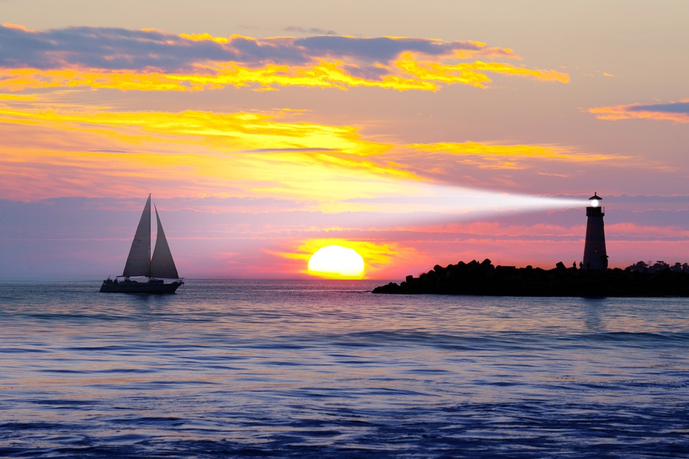 Sunset at sea, a sailboat and a shining lighthouse.
