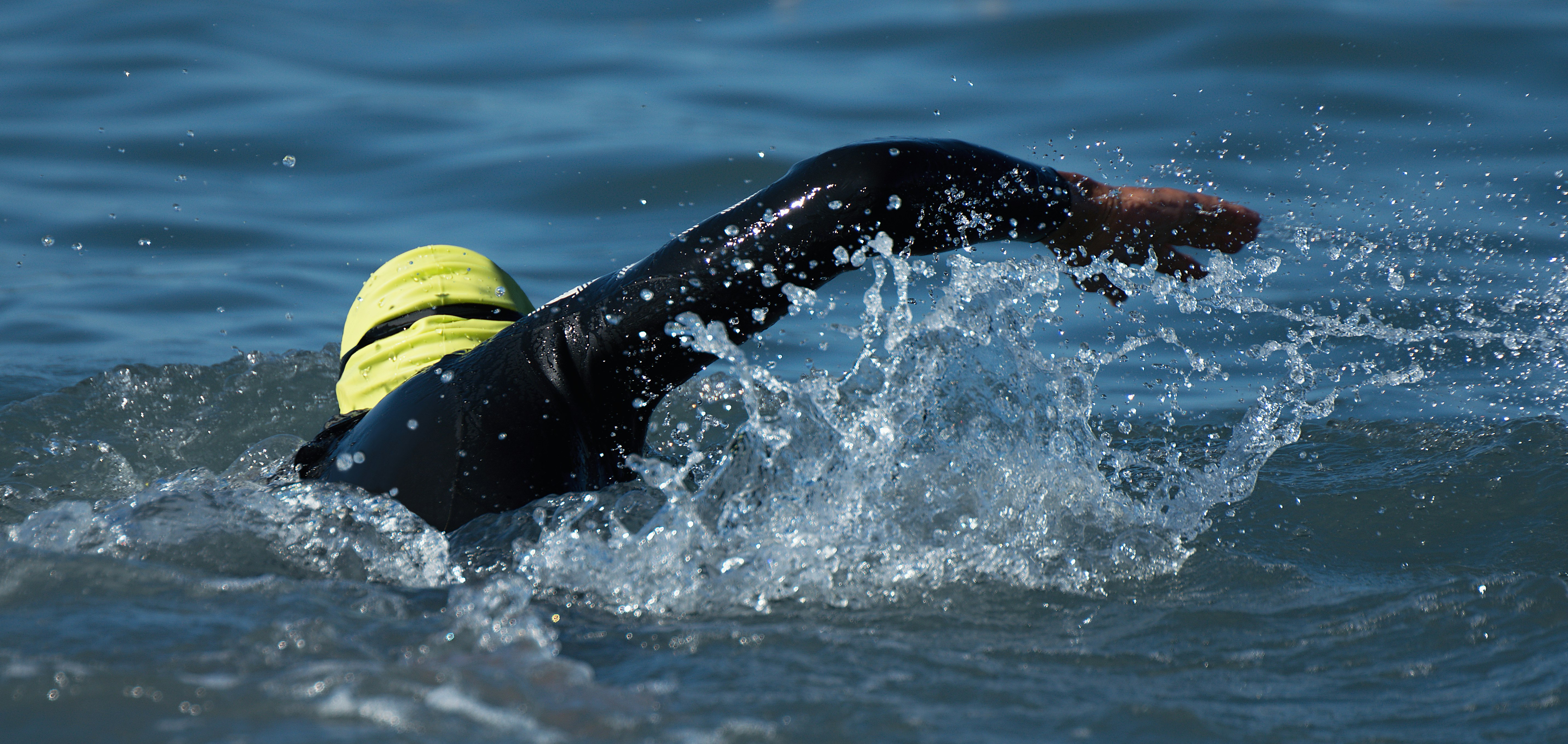 Schwimmerin mit grauer Kappe schwimmt im türkisfarbenen Meerwasser der Insel. Frauensport im Sommer