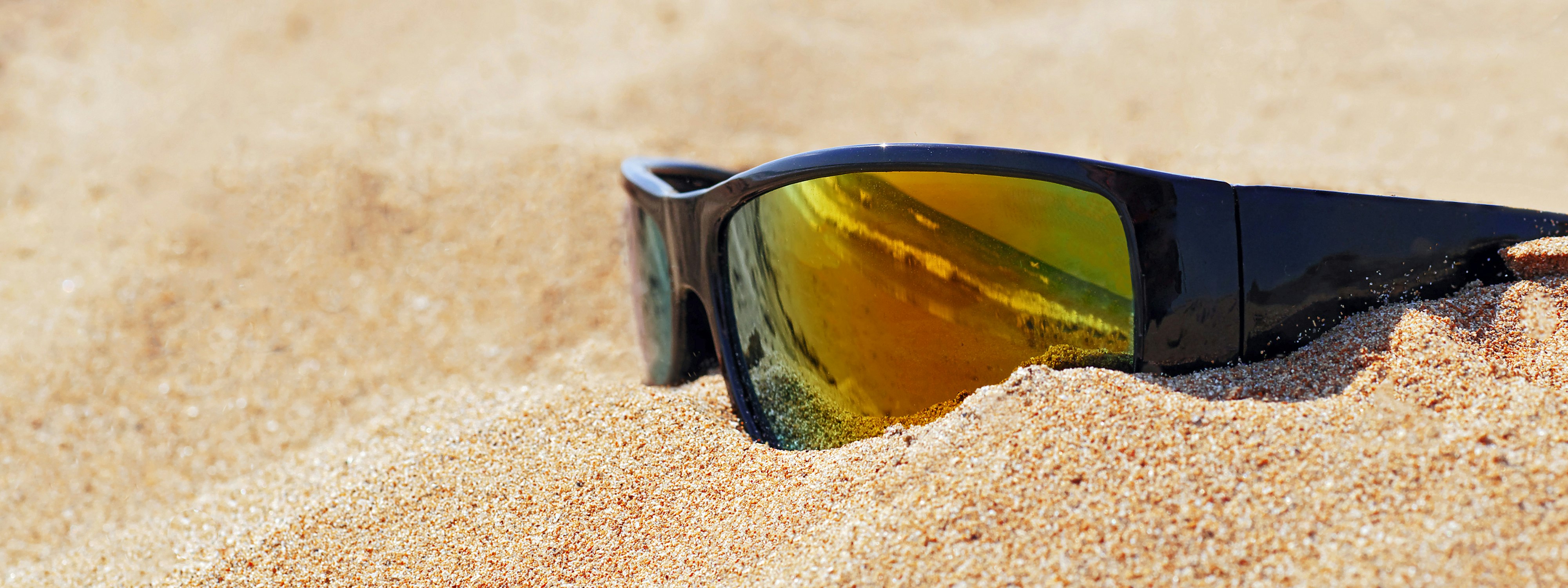 Nahaufnahme einer spiegelnden Sonnenbrille auf Sand am Strand, die Meereswellen reflektiert, geeignet für Header oder Banner