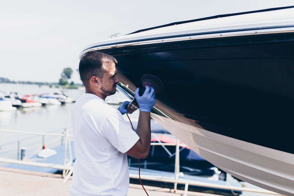 A man repairs the damaged gelcoat on the hull.