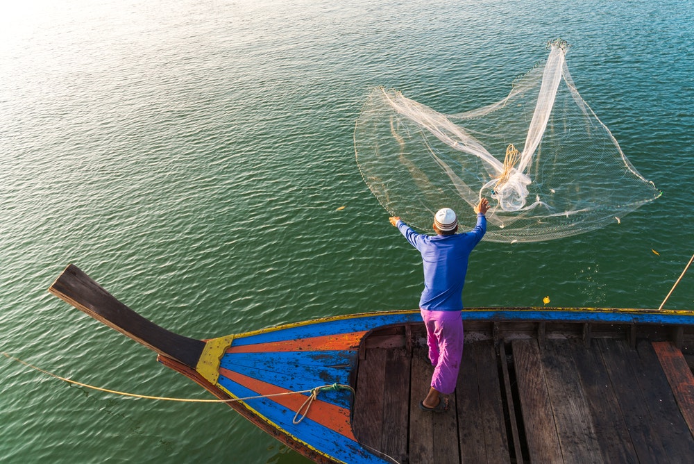 Ein Fischer in Thailand wirft ein Fischernetz ins Wasser